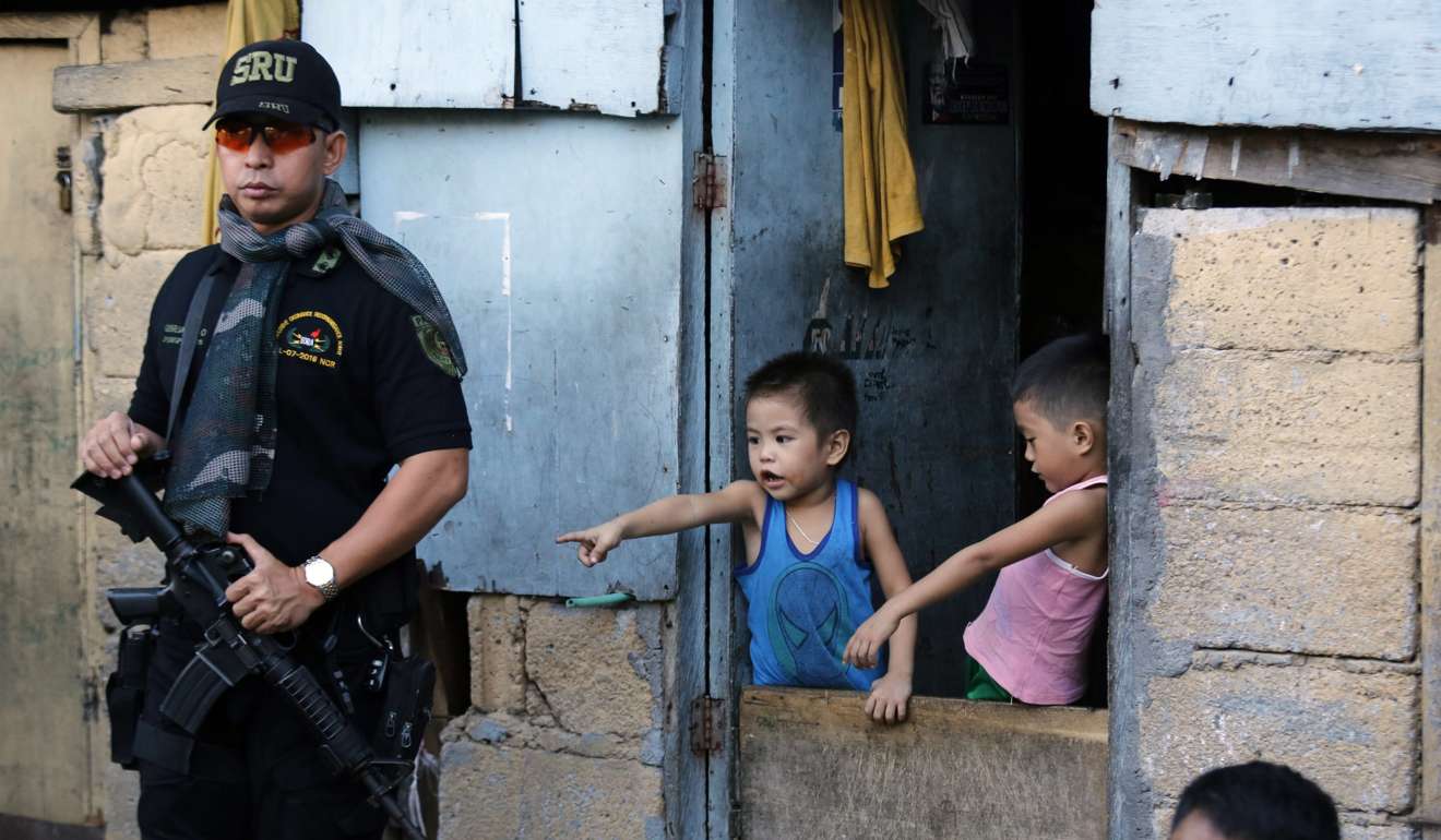 An armed Filipino member of the Special Weapons and Tactics team stands guard as children look on during an anti-drug operation. Photo: EPA