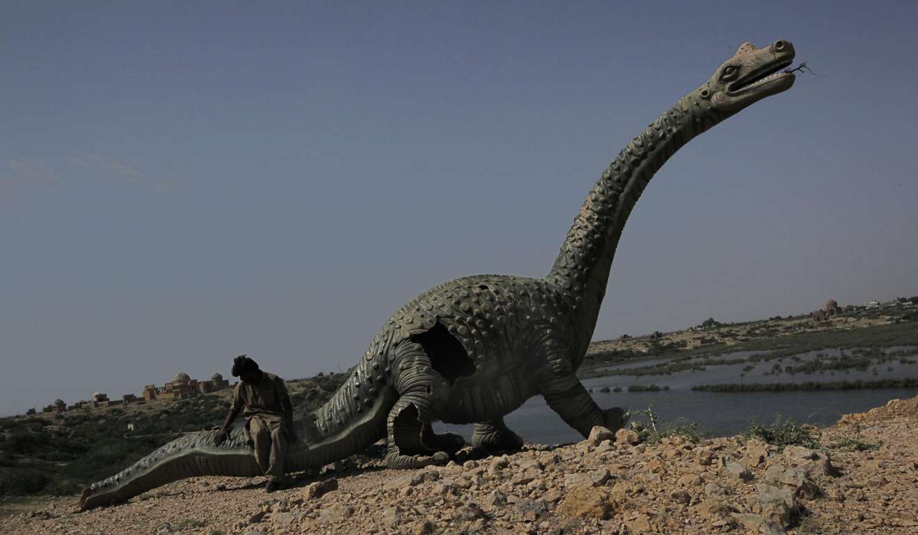 A Pakistani man, who survived floods sits on a dinosaur model in a flooded area in Makli, Sindh province. Photo: AP