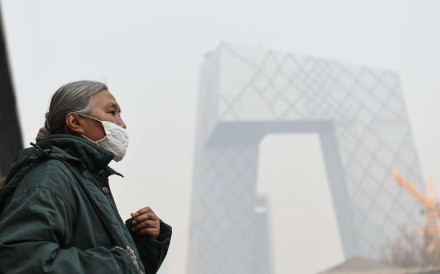 A woman wearing a mask walks past Guomao Bridge in Beijing, with the CCTV building behind her. Photo: Xinhua