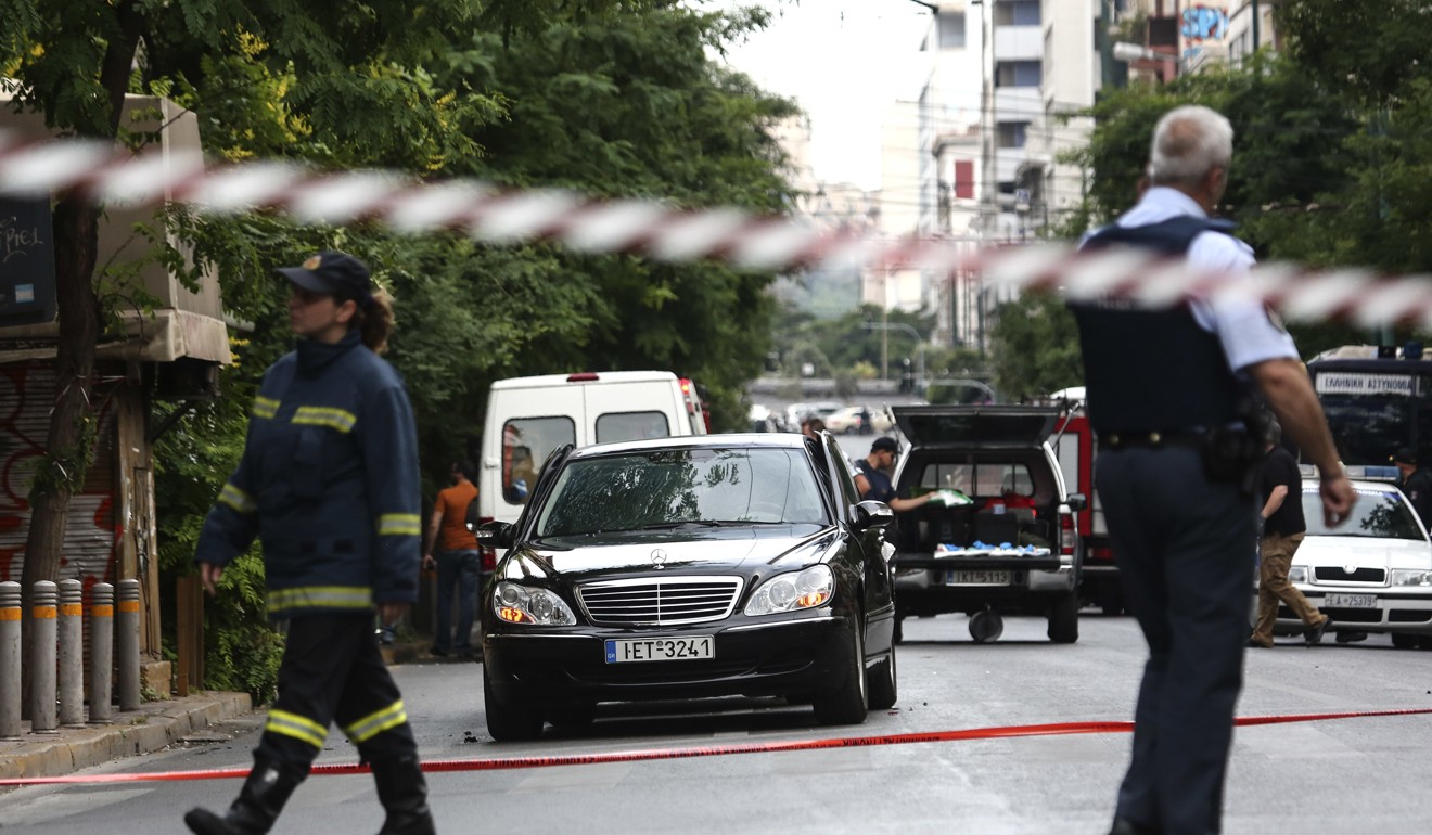 Members of the Greek emergency services walk by the car of former prime minister Lucas Papademos in central Athens. Photo: AP