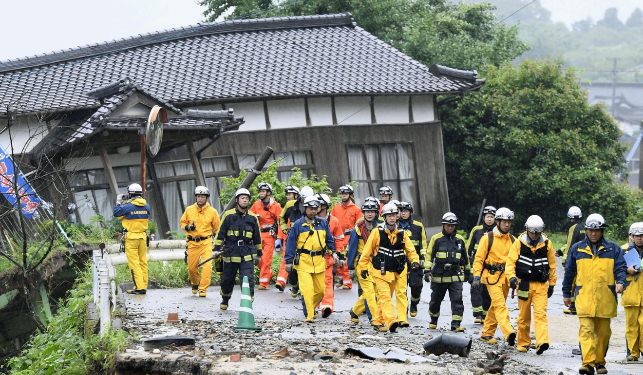 Firefighters walk on the damaged road following the flooding caused by heavy rain in Asakura. Photo: Kyodo