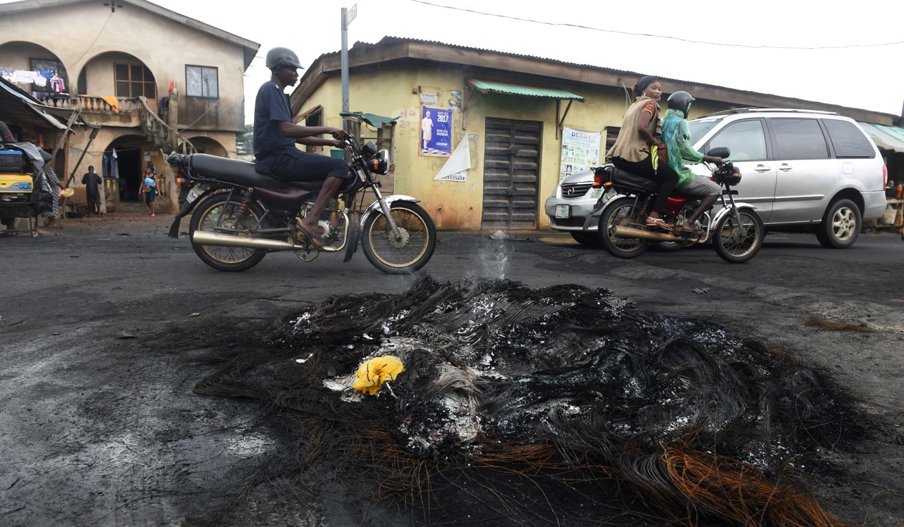 Taxi motorcyclists drive past smouldering bonfires lit by vigilantes to watch over Owode Onirin in Lagos, on July 7. Photo: AFP