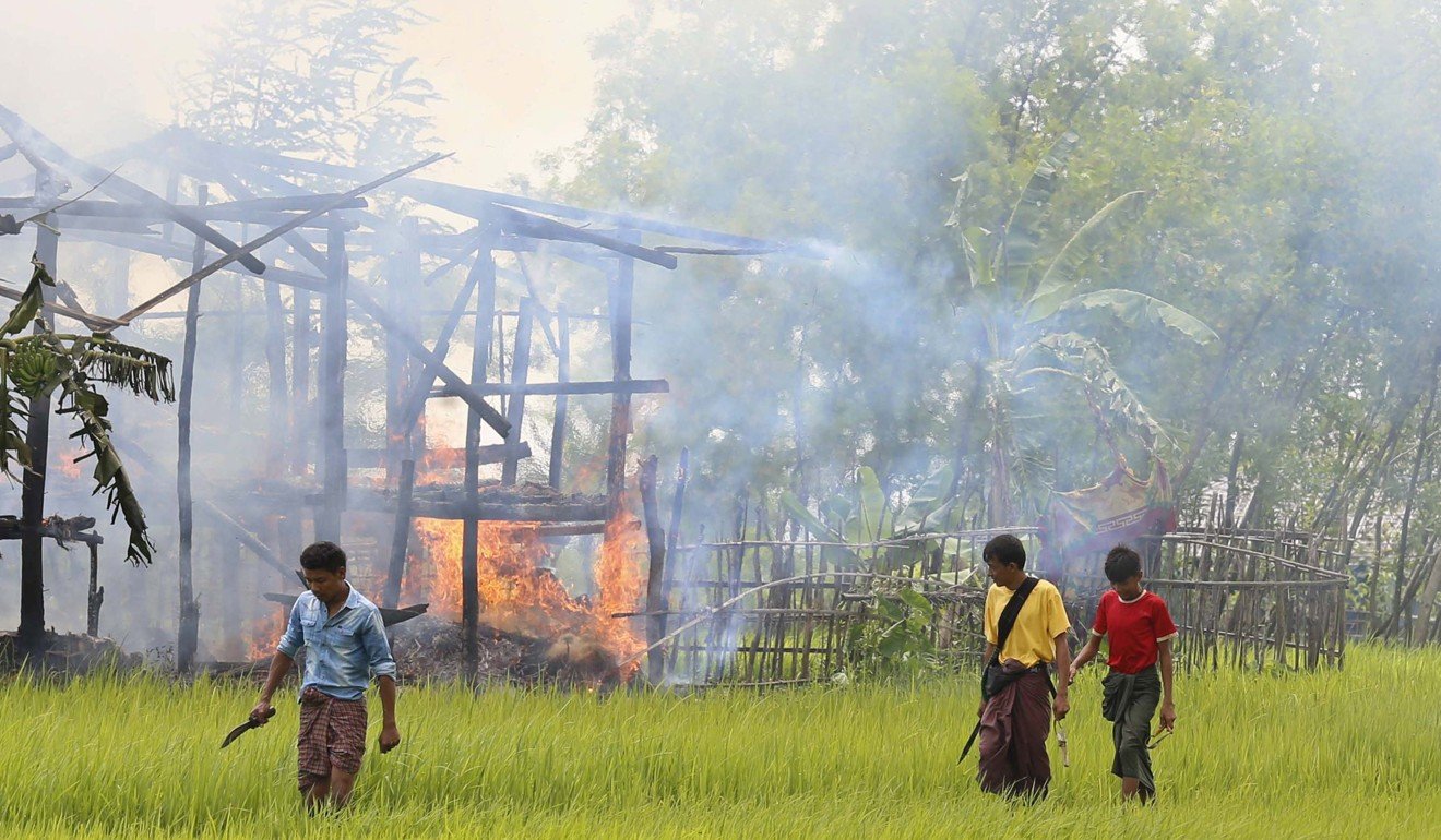 People reportedly from the Rakhine ethnic group hold knives and sling shots as they walk near a burning house at the Gawdu Thara village in Maungdaw township, Rakhine State. Photo: EP