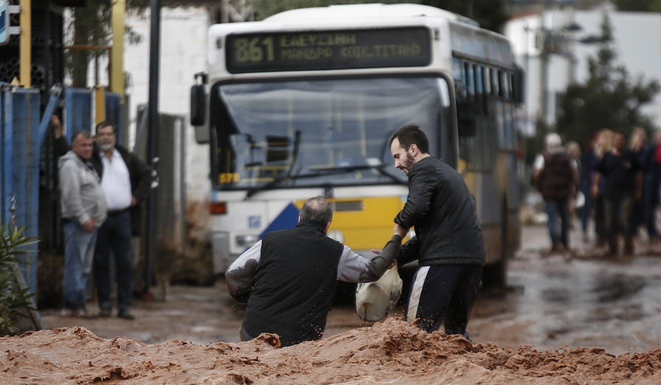 People struggle to walk in a flooded street following a heavy rainfall in the town of Mandra, not far from Athens. Photo: Xinhua