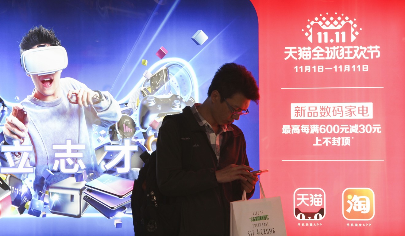 A man checks his smartphone in front of a Tmall Singles' Day Global Shopping Festival poster at a subway station in Shanghai on November 11, 2017. The three-year cooperation between the Ford Motor Company and Alibaba Group Holding will explore a range of car retail opportunities through online shopping platform Tmall. Photo: Simon Song