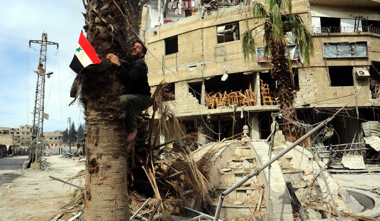 A man climbs a tree to hoist the Syrian flag in the town of Saqba in the capital Damascus' eastern Ghouta after the army liberated it on March 18, 2018. Syrian President Bashar al-Assad visited eastern Ghouta on Sunday, as the army has liberated 80 per cent of that area from the rebels. Photo: Xinhua