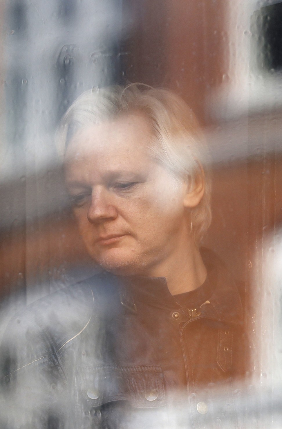 Julian Assange looks out the window from the Ecuadorean embassy in London on May 19, 2017. Photo: AP 