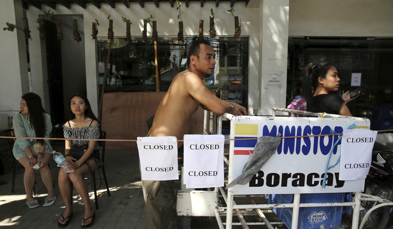 A worker waits outside a shop that has closed a day before the government temporarily closes the island. Photo: AP