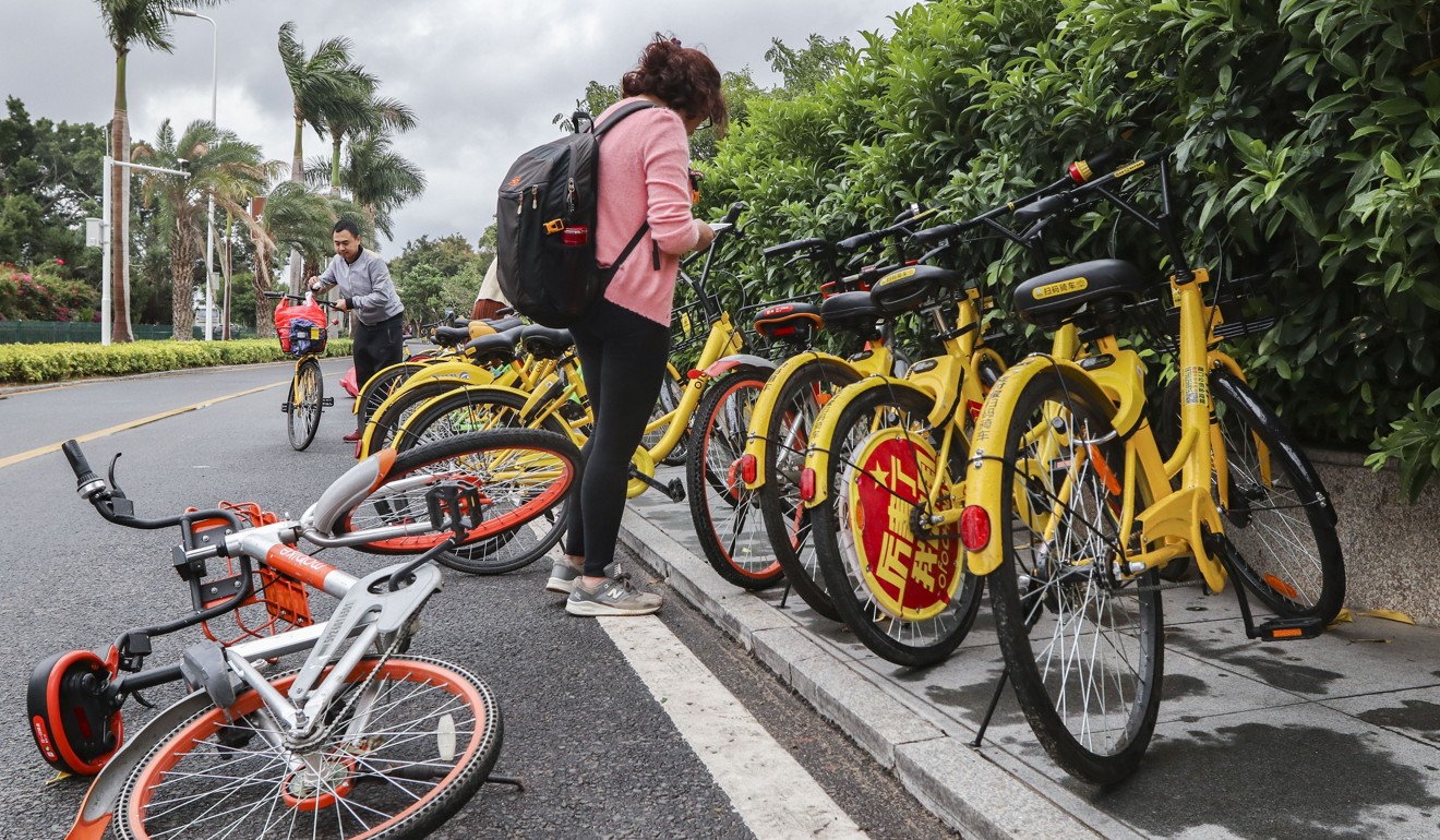 A woman prepares to ride OFO, a bike-sharing bicycle while Mobike, another bike-sharing company lays on the floor in Xiamen, Fujian Province in southerneastern China. Photo: SCMP