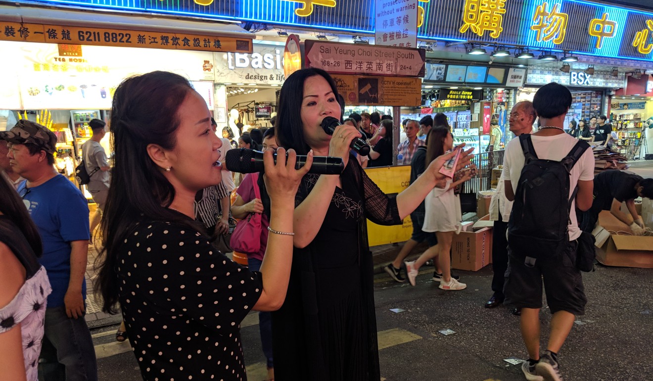 Singer Ling (right) holds cash tips whilst performing on Sai Yeung Choi Street South. Photo: Sum Lok-kei