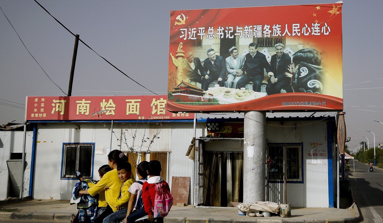 At Unity New Village, Hotan, Xinjiang, a Uygur and schoolchildren past a sign showing China's President Xi Jinping joining hands with Uygur elders. Photo: AP
