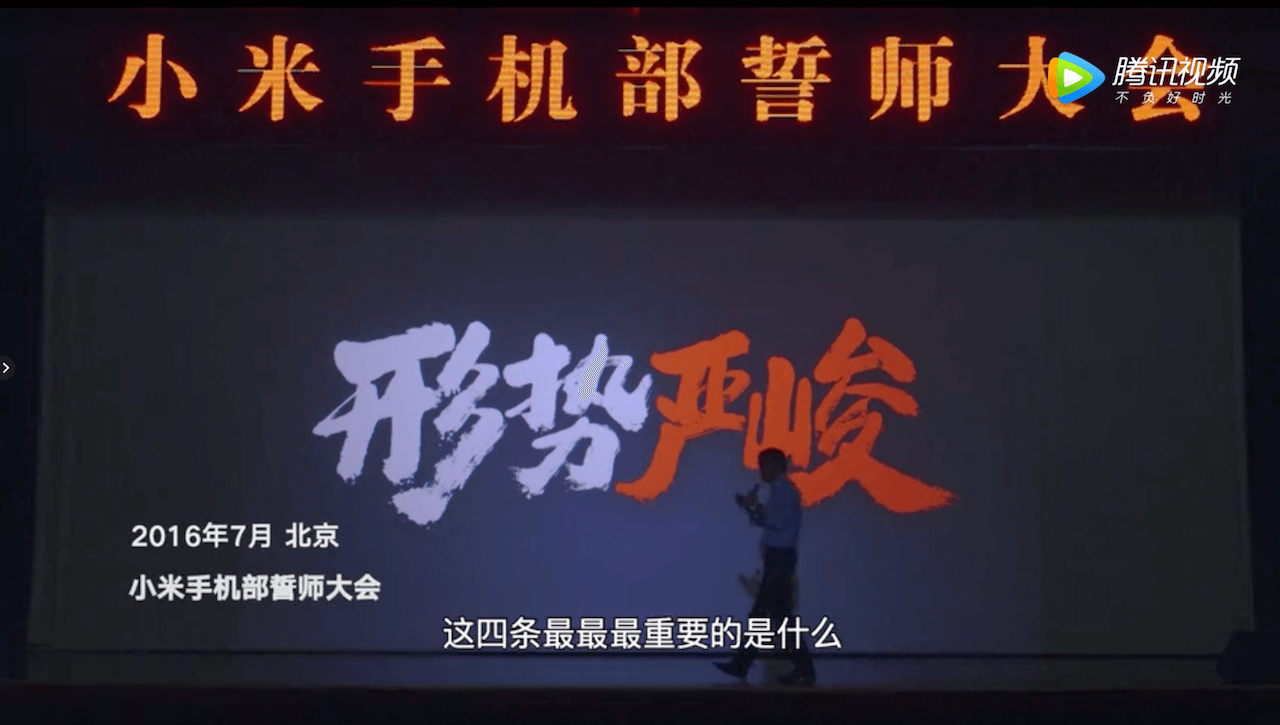 Lei Jun on stage rallying his smartphone employees in July 2016. The words on the screen read, “The situation is tough.” (Picture: Xiaomi/Tencent Video)